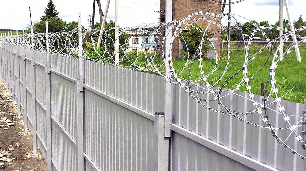Спиральный барьер безопасности на прямых кронштейнах из уголка, закрепленных на заборе из профлиста